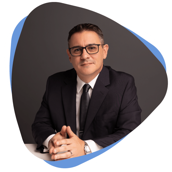 Man in a suit and tie with glasses, seated against a dark background.