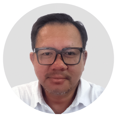 A man with short dark hair, wearing glasses and a white shirt, against a neutral background.