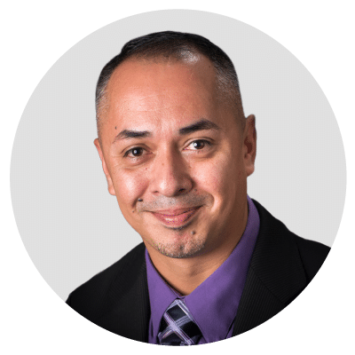 Man in a suit and purple shirt smiling at the camera.