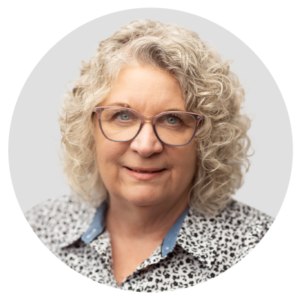 A person with curly gray hair and glasses, wearing a patterned shirt.