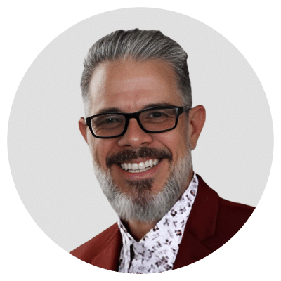 Alt text: Man with gray hair and glasses wearing a red jacket and patterned shirt, smiling.