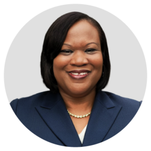 A person smiling, wearing a dark blue suit against a plain background.