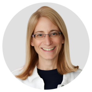 A person with long blond hair and glasses, smiling, wearing a black shirt with a white jacket.