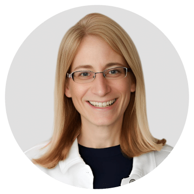 A person with long blond hair and glasses, smiling, wearing a black shirt with a white jacket. A person with long blond hair and glasses, smiling, wearing a black shirt with a white jacket.