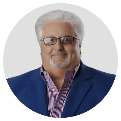 A man with white hair and glasses wearing a blue suit jacket and striped shirt.