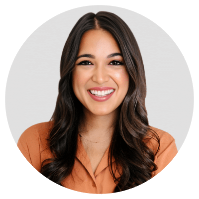 A person with long, dark hair smiling and wearing a brown shirt against a plain background.