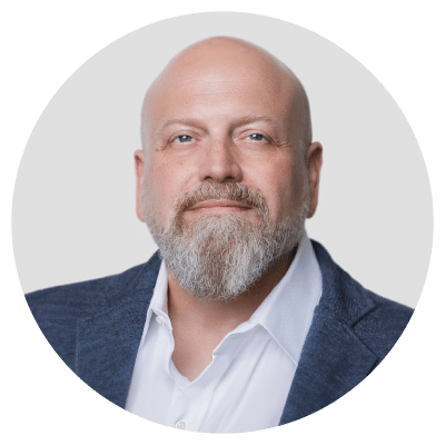 Man with a bald head and a gray beard wearing a white shirt and dark suit jacket.