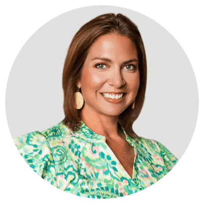 A woman with shoulder-length brown hair wearing a colorful patterned blouse and gold earrings, smiling against a plain background.