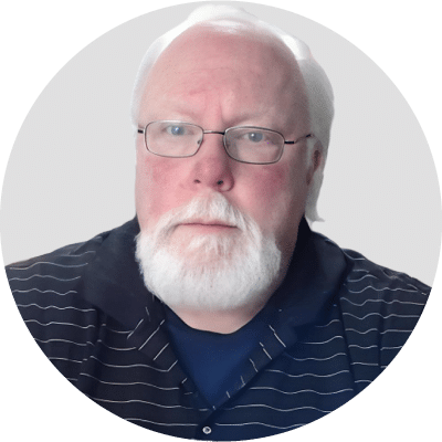 A bearded man with glasses wearing a striped polo shirt against a plain background.