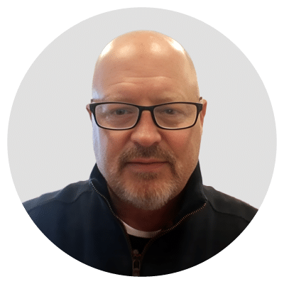 A person with glasses, a bald head, a goatee, and wearing a black jacket.