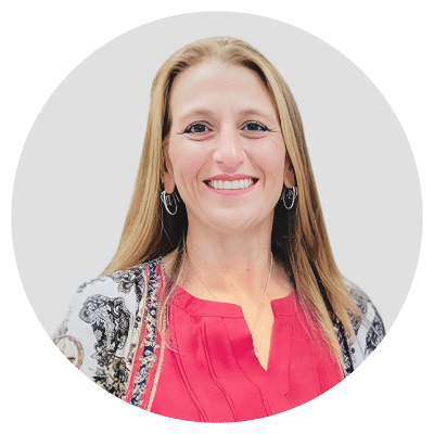 A woman with long hair, wearing a red blouse and patterned jacket, smiling against a light background.