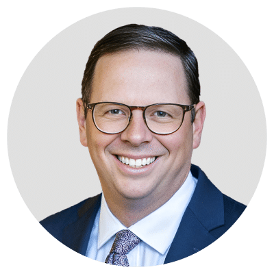 A smiling man wearing glasses, a suit, and a tie.